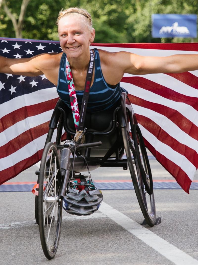A female wheelchair racer holds up an American flag