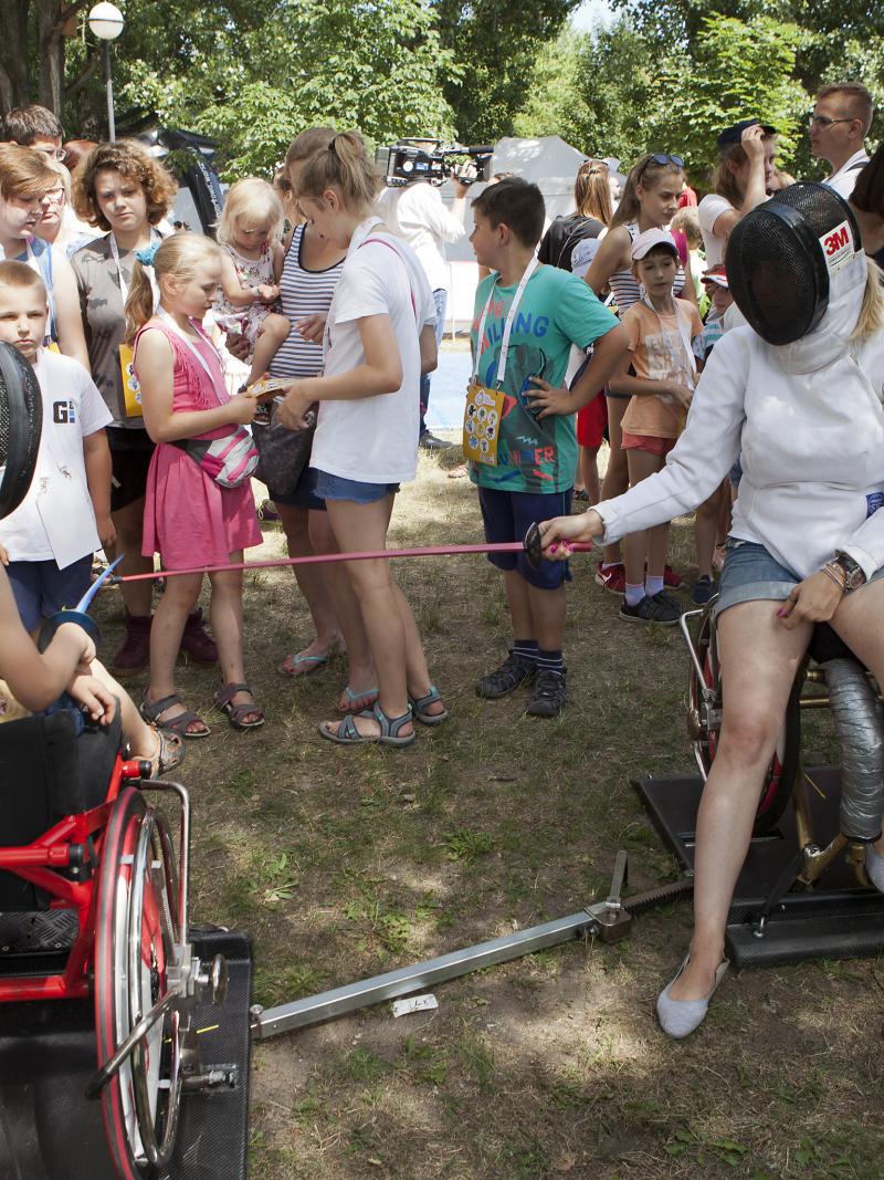 Group of children watching two people practicing wheelchair fencing