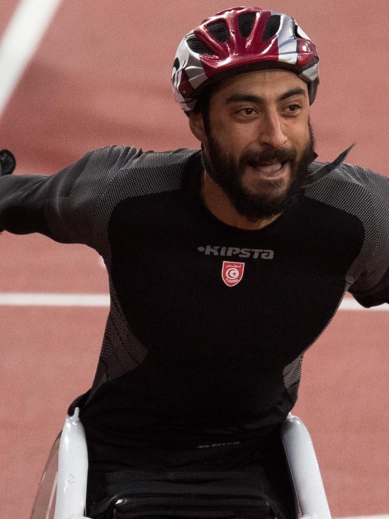 a male wheelchair racer throws his arms up in celebration
