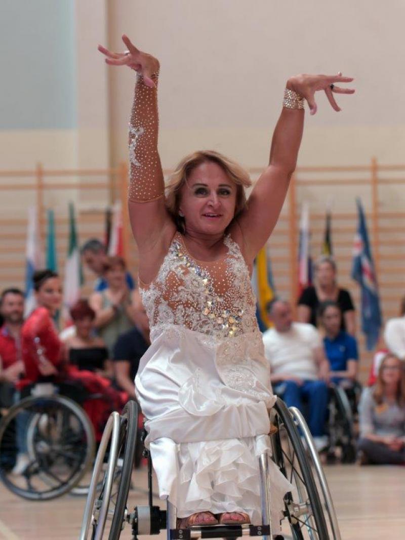 a female wheelchair dancer raises her arms above her head as part of a move