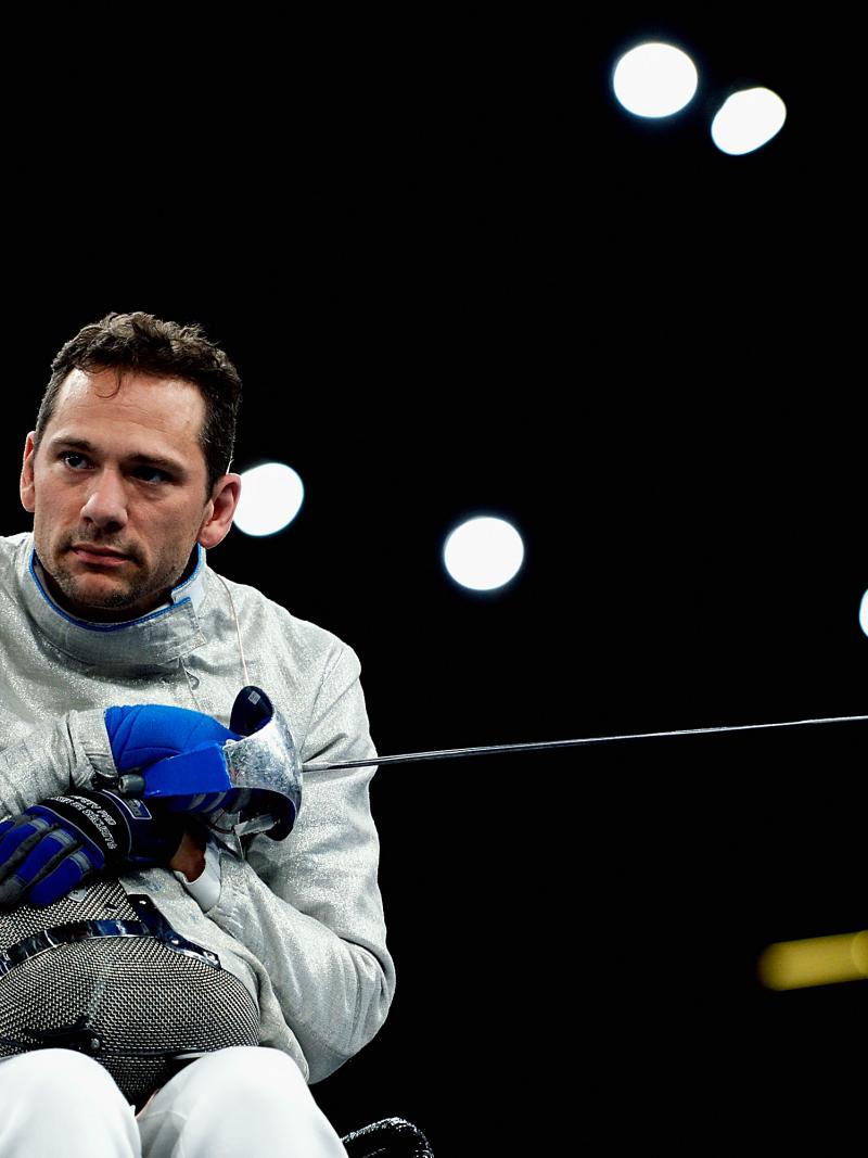a male wheelchair fencer holding a foil and his helmet