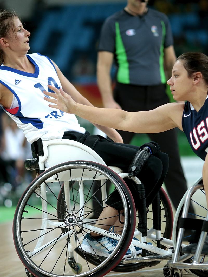Woman in wheelchair holding a basketball while another tries to defend her