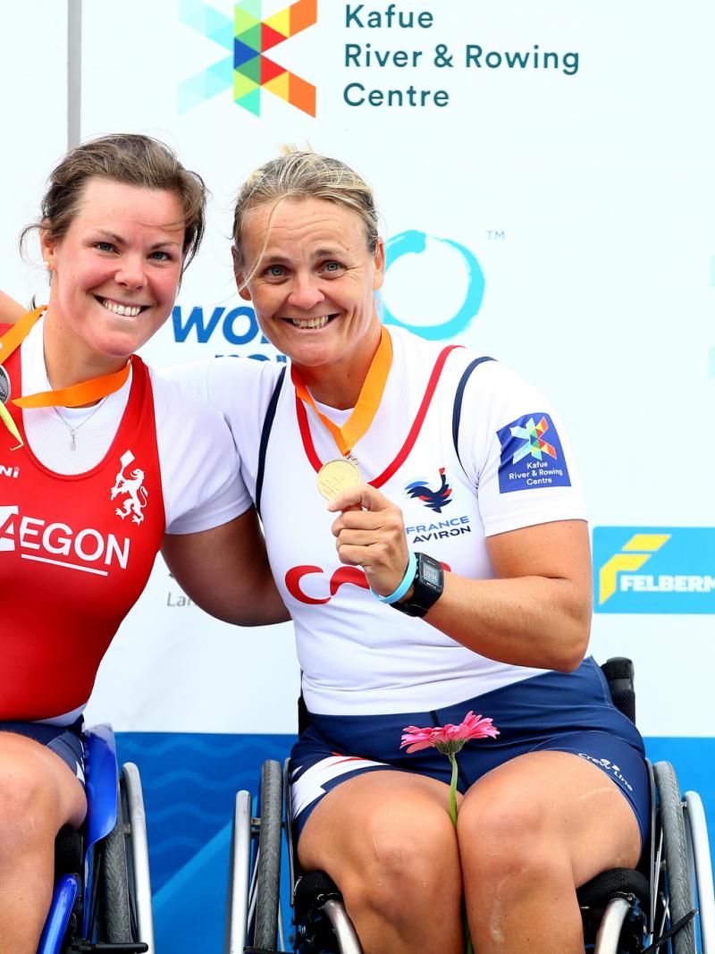 two female Para rowers in wheelchairs hug on the podium