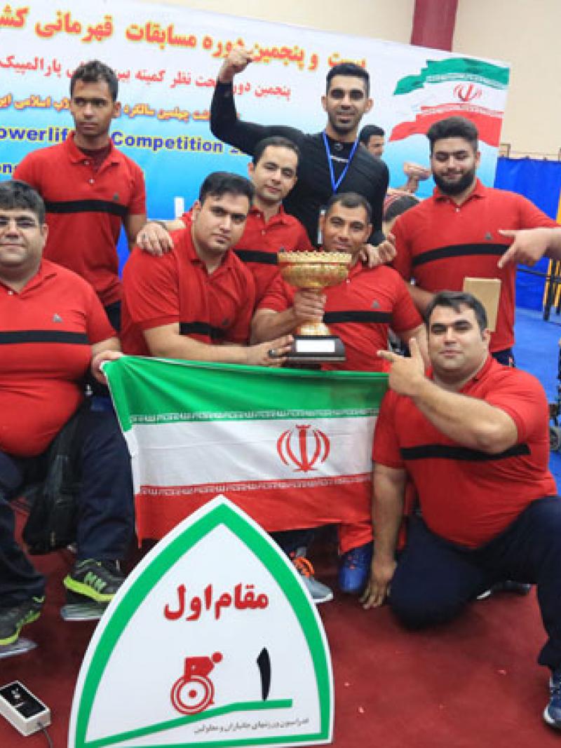 a group of male powerlifters holding an Iran flag and a trophy