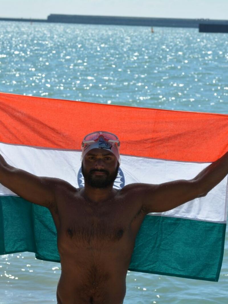 a male Para swimmer holds up in India flag beside the sea