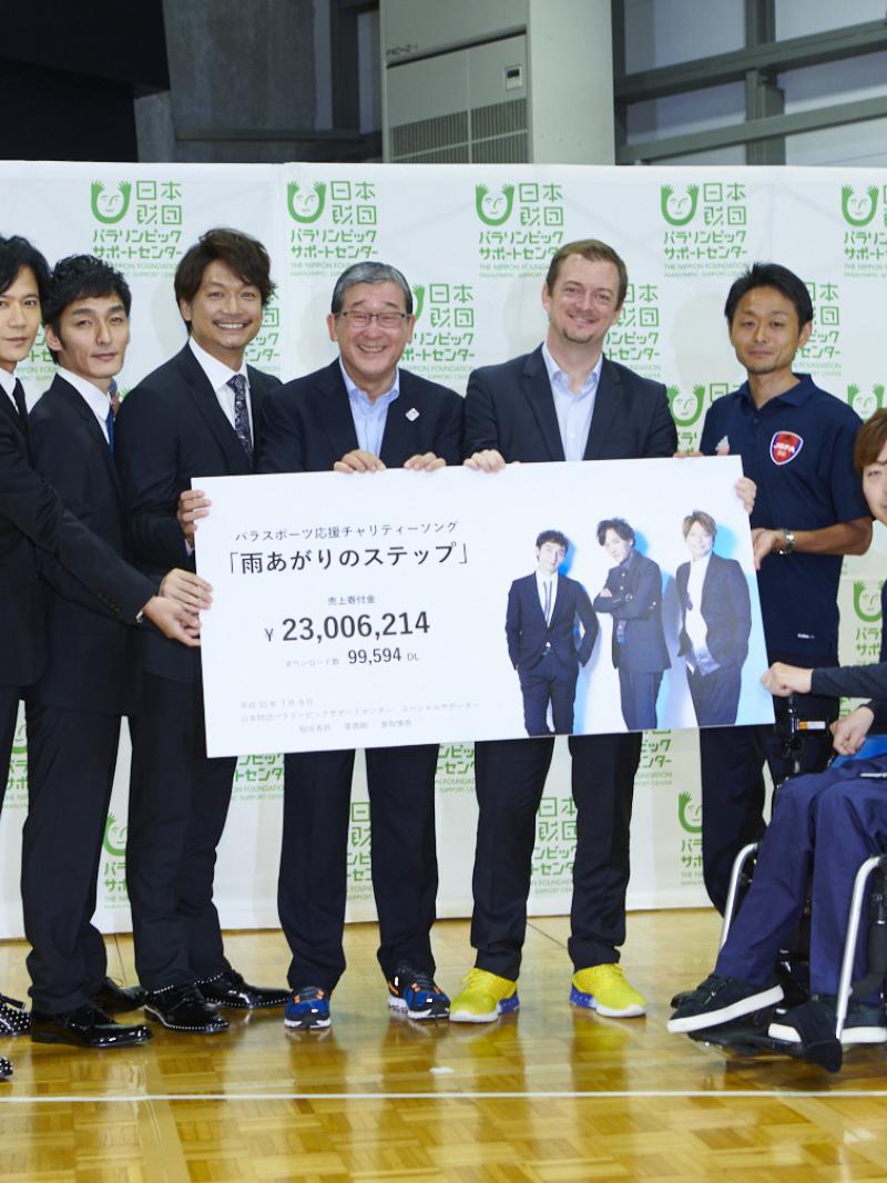 Six men standing and one in a wheelchair holding a cheque 