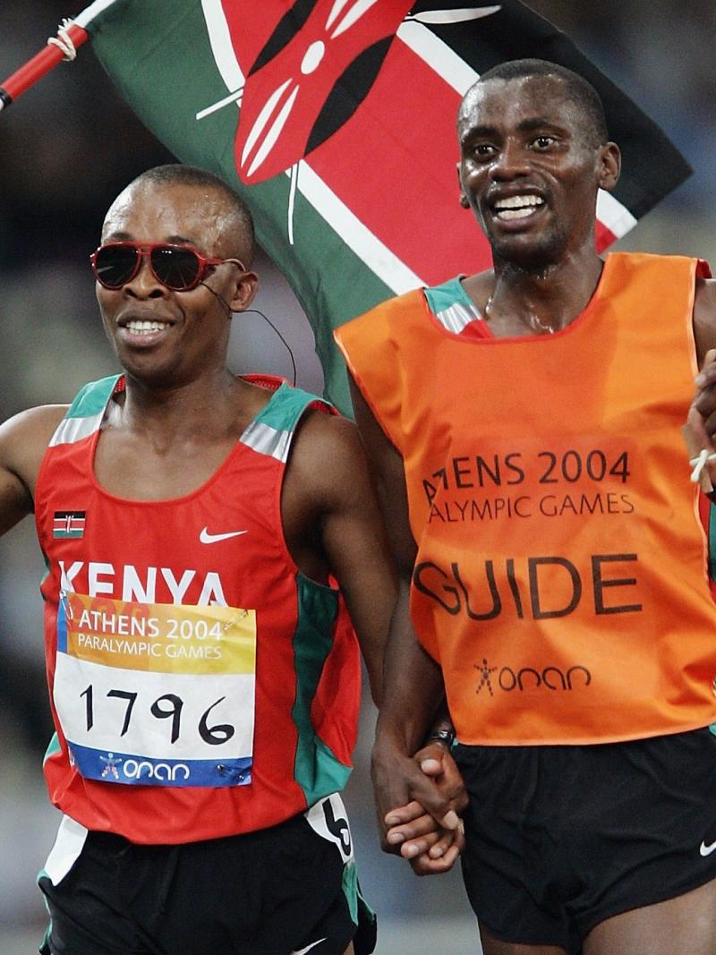 blind male runner Henry Wanyoike and his guide on a track carrying the Kenya flag