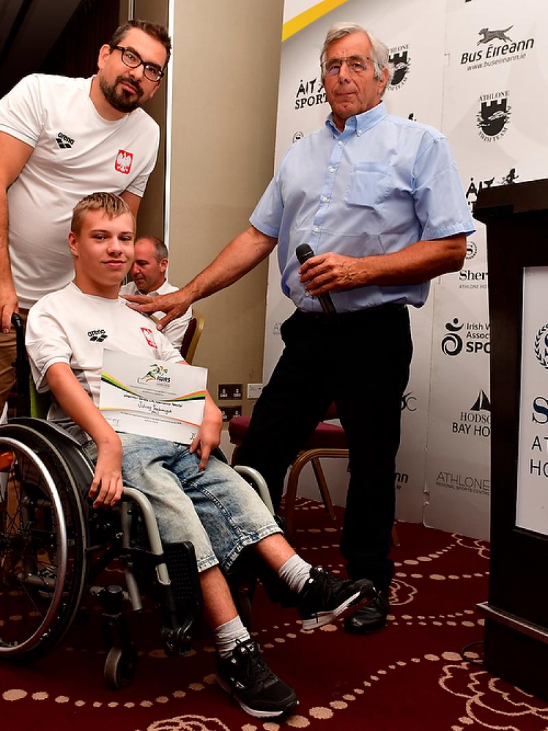 Polish male swimmer Juliusz Trochimczuk in a wheelchair receives an award from two men