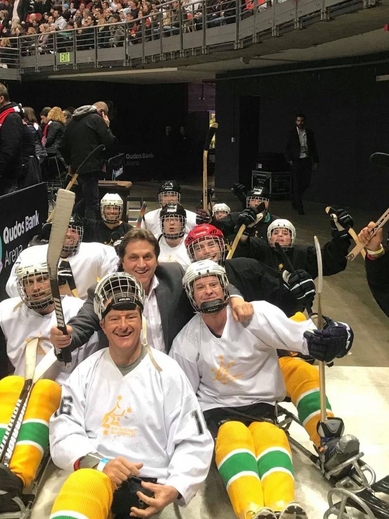 Fifteen people on sledges with Para ice hockey gear posing for a picture