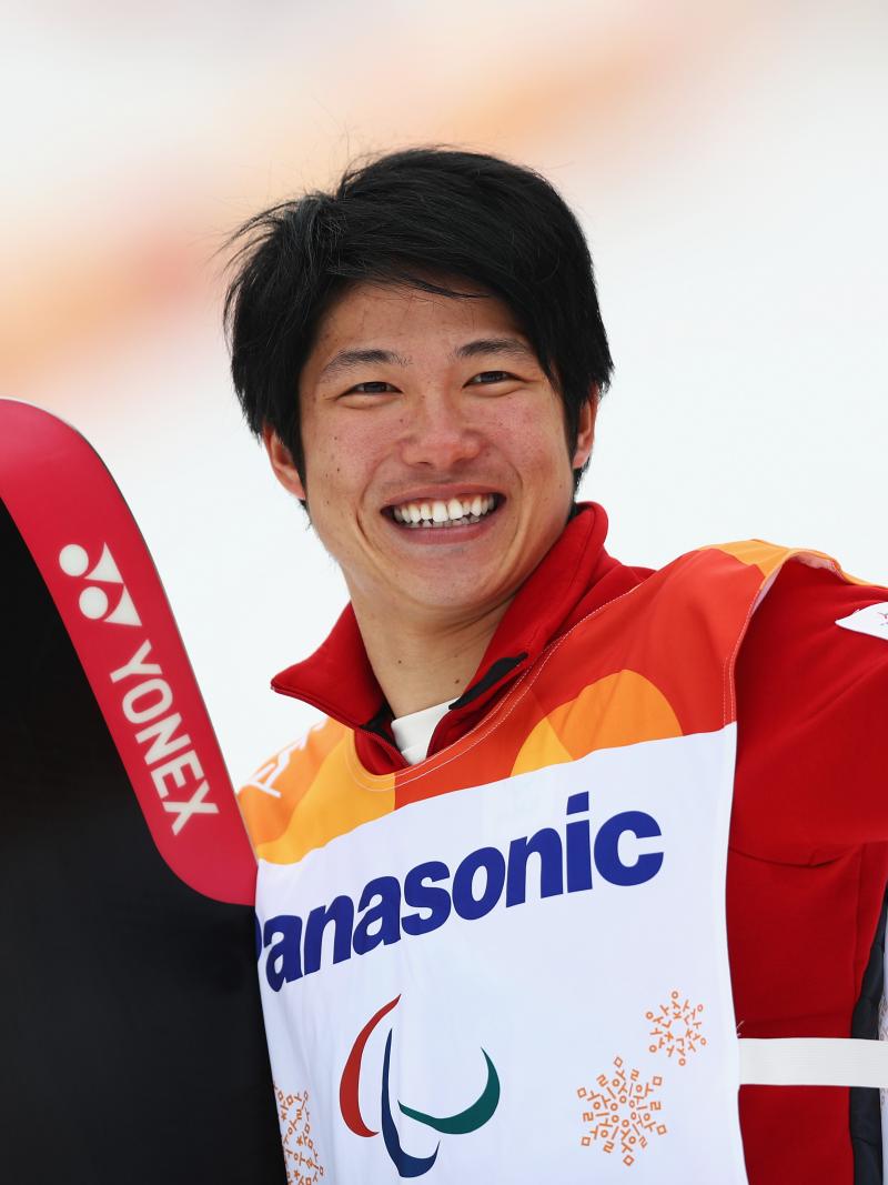 male Para snowboarder Gurimu Narita holds his snowboard and waves to fans