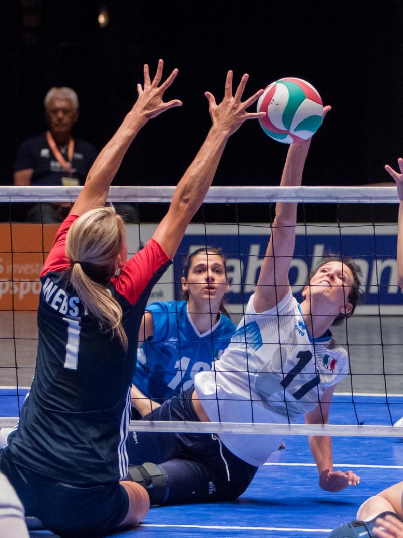 a group of female sitting volleyballers blocking the ball at the net