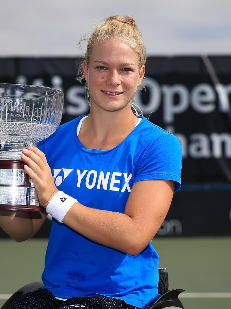 Female wheelchair tennis player Diede de Groot smiles and lifts a glass trophy