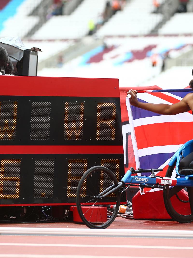 Female wheelchair racer Kare Adenegan holds up a British flag next to the display of her world record time