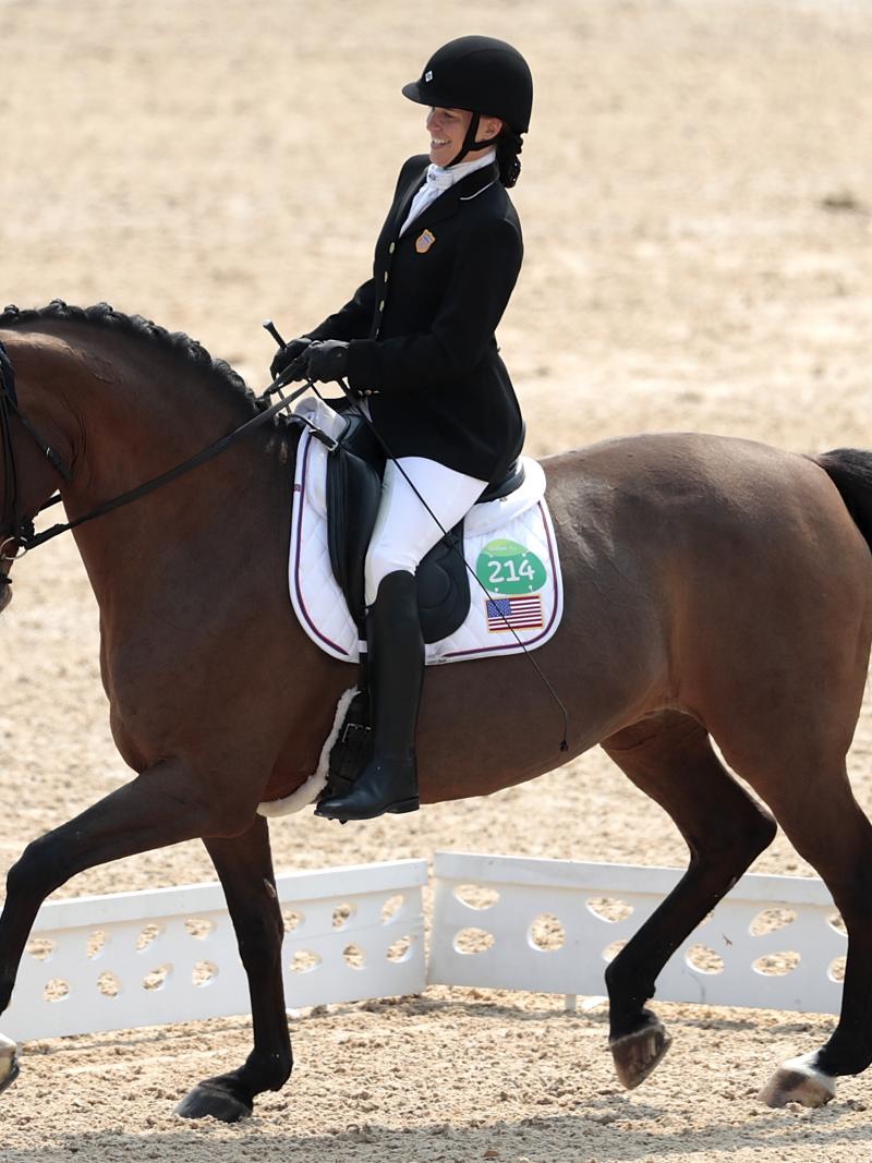 female Para equestrian rider Rebecca Hart competes on a horse in a dressage arena