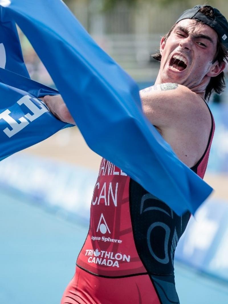 male Para triathlete Stefan Daniel rips the tape at the finishing line as he crosses to win the race
