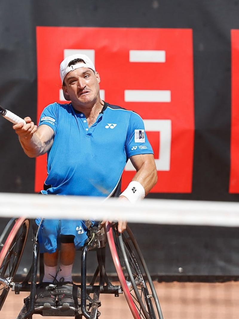 male wheelchair tennis player Gustavo Fernandez plays a forehand on a clay court