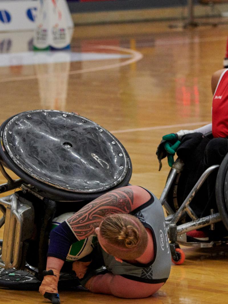 a Danish wheelchair rugby player on the ground after a tackle from a New Zealand wheelchair rugby player