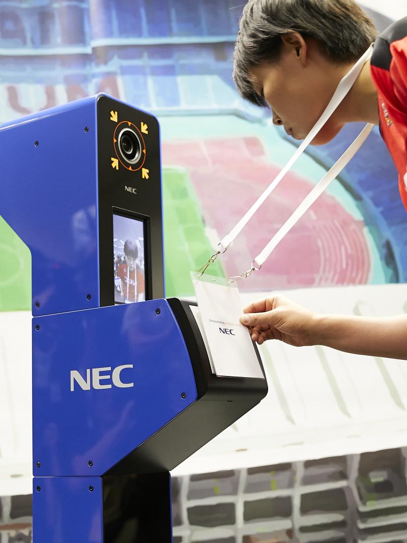 a person looks into a camera while displaying their accreditation in a simulation of the Tokyo 2020 system