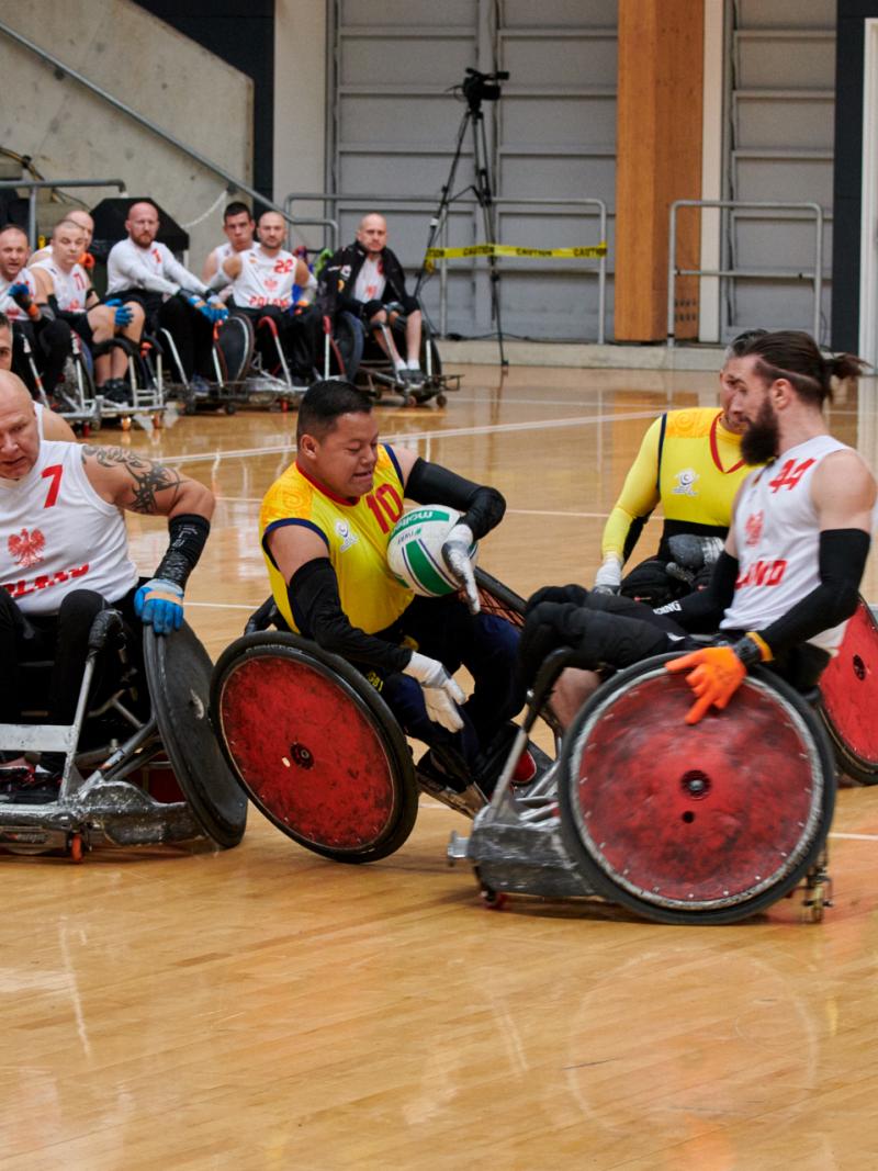 two Colombian wheelchair rugby players tackling a Polish player for the ball