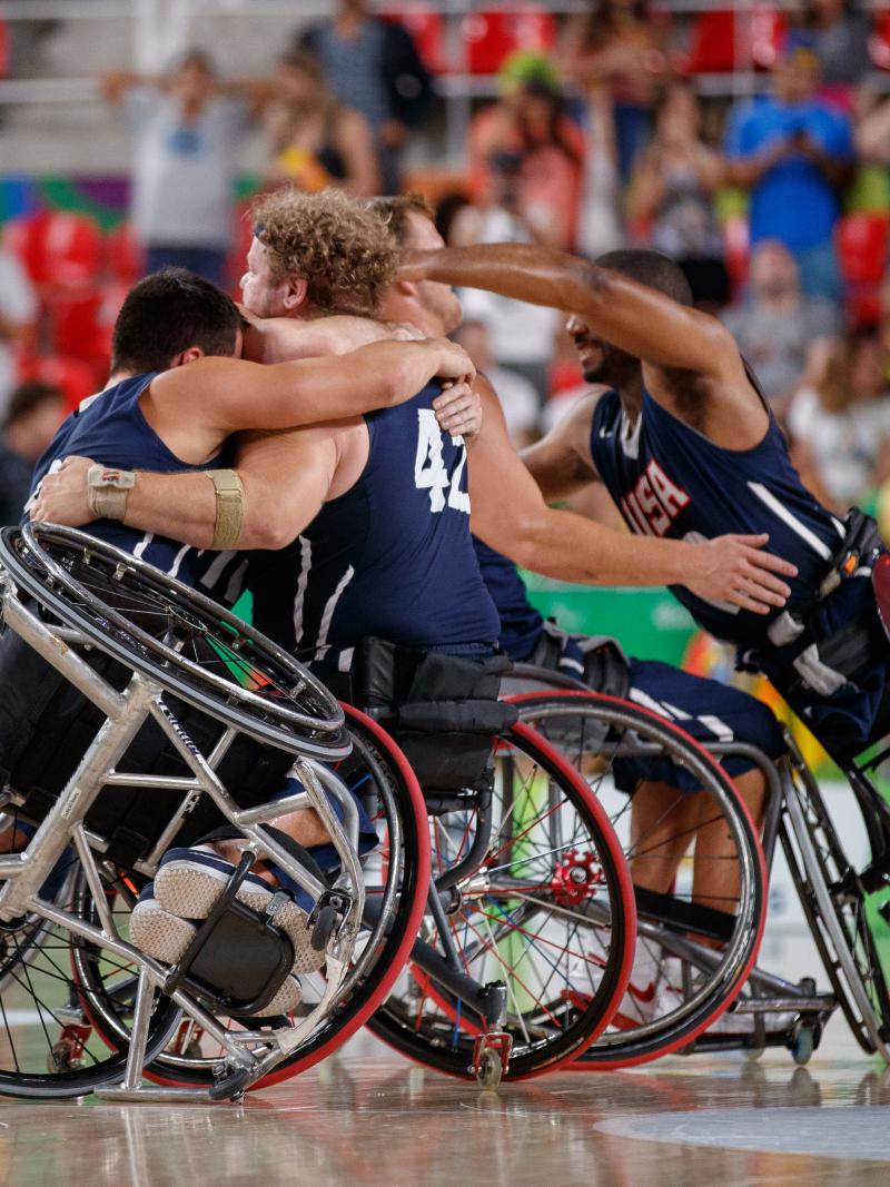 a group of male wheelchair basketballers from the USA hug on the court