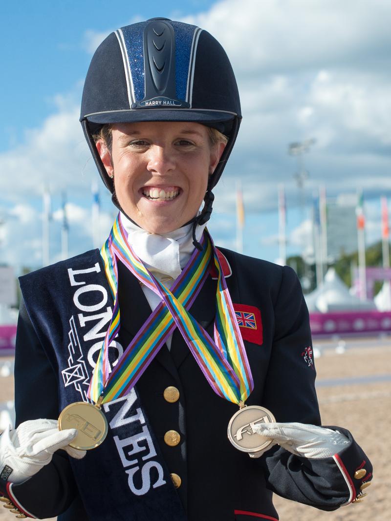 female Para equestrian rider Erin Orford smiles and holds up two gold medals around her neck