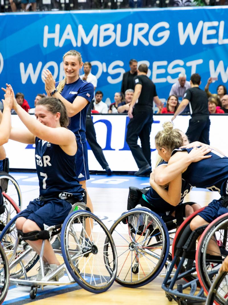 a group of female British wheelchair basketballers hugging and smiling on court