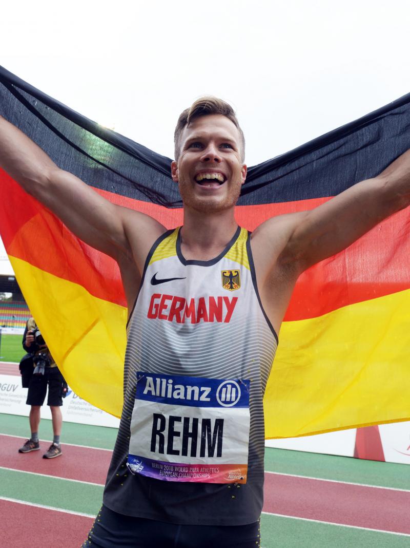 male long jumper Markus Rehm holding up the Germany flag and smiling