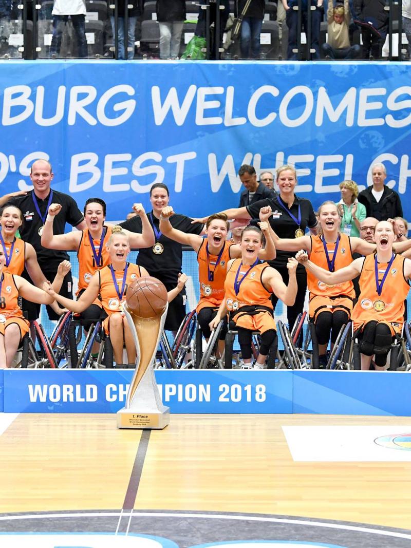 A group of women in organge vests celebrate with a large trophy after winning the world title