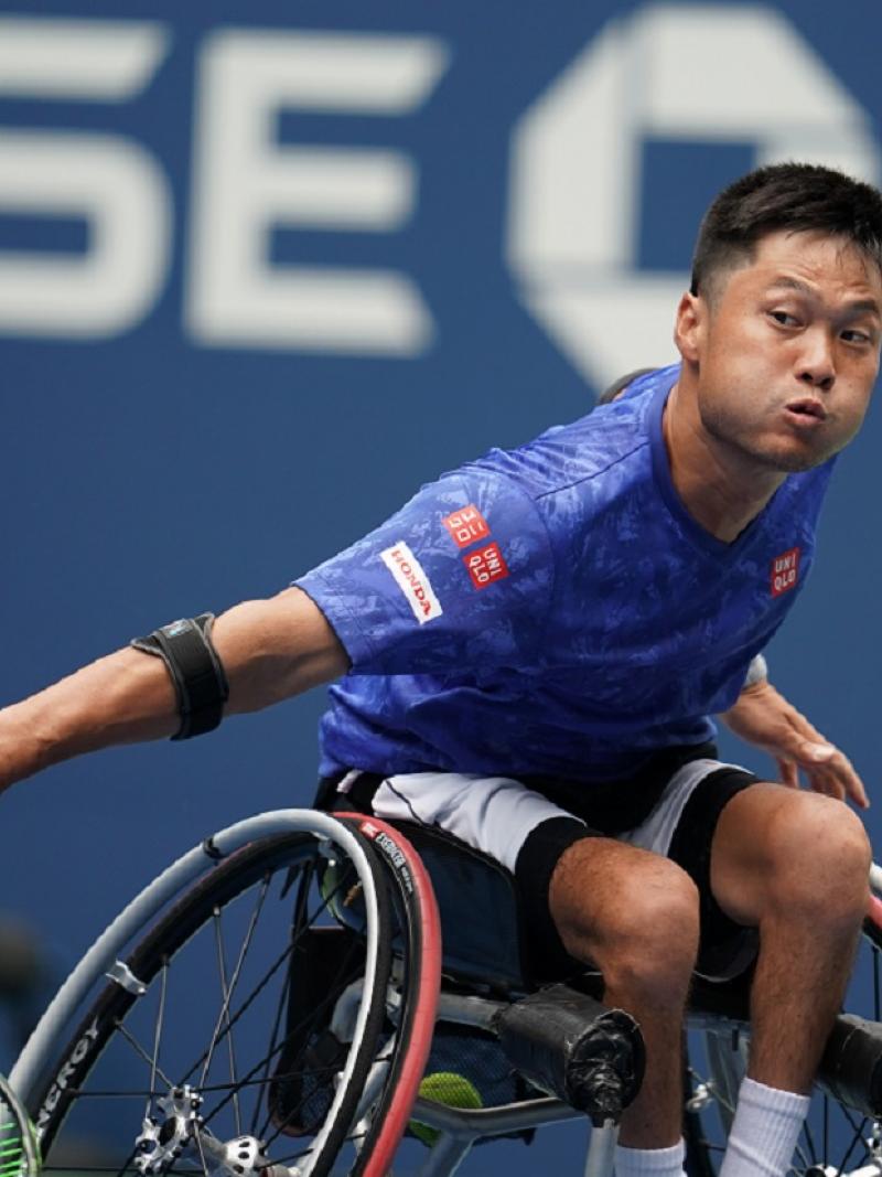 Japanese man in wheelchair reaches to his tennis ball