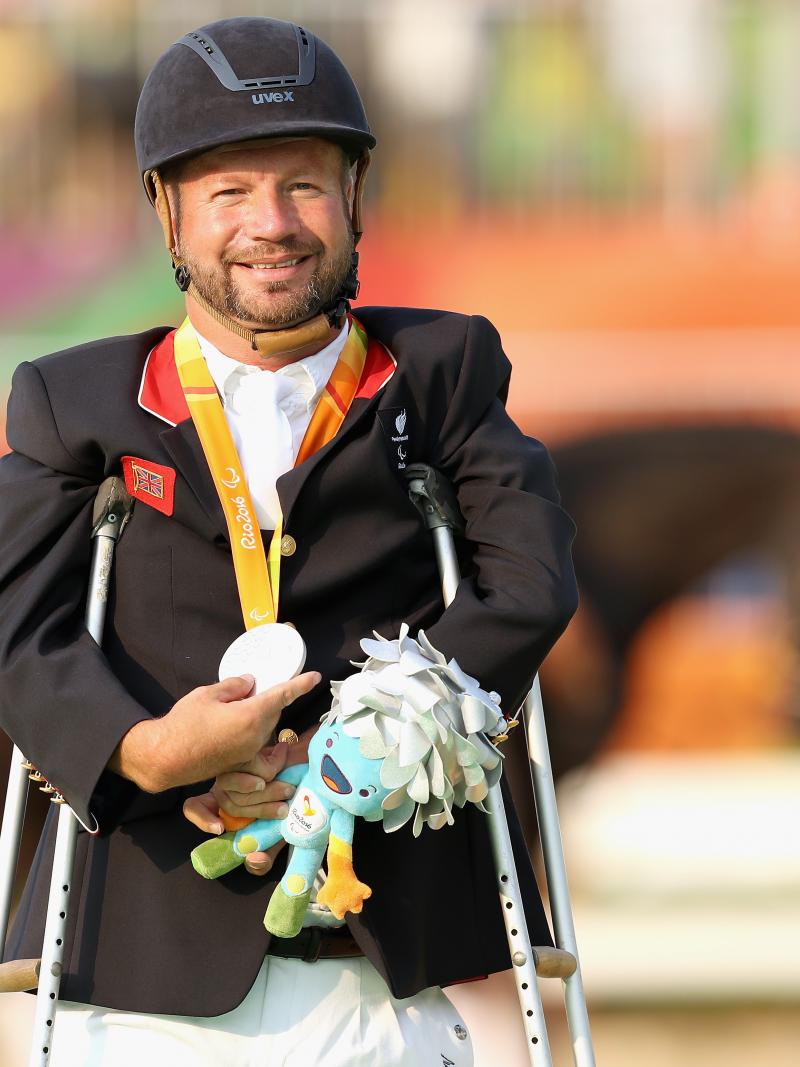male Para equestrian rider Lee Pearson standing on crutches holding a medal