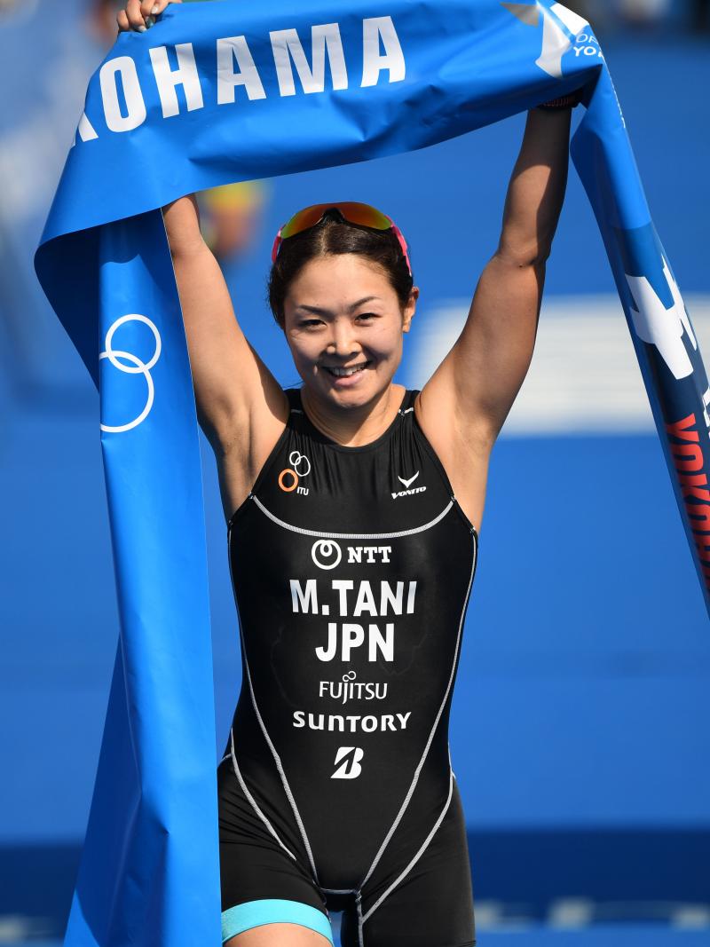 female Para triathlete Mami Tani holds up the finish tape as she crosses the line