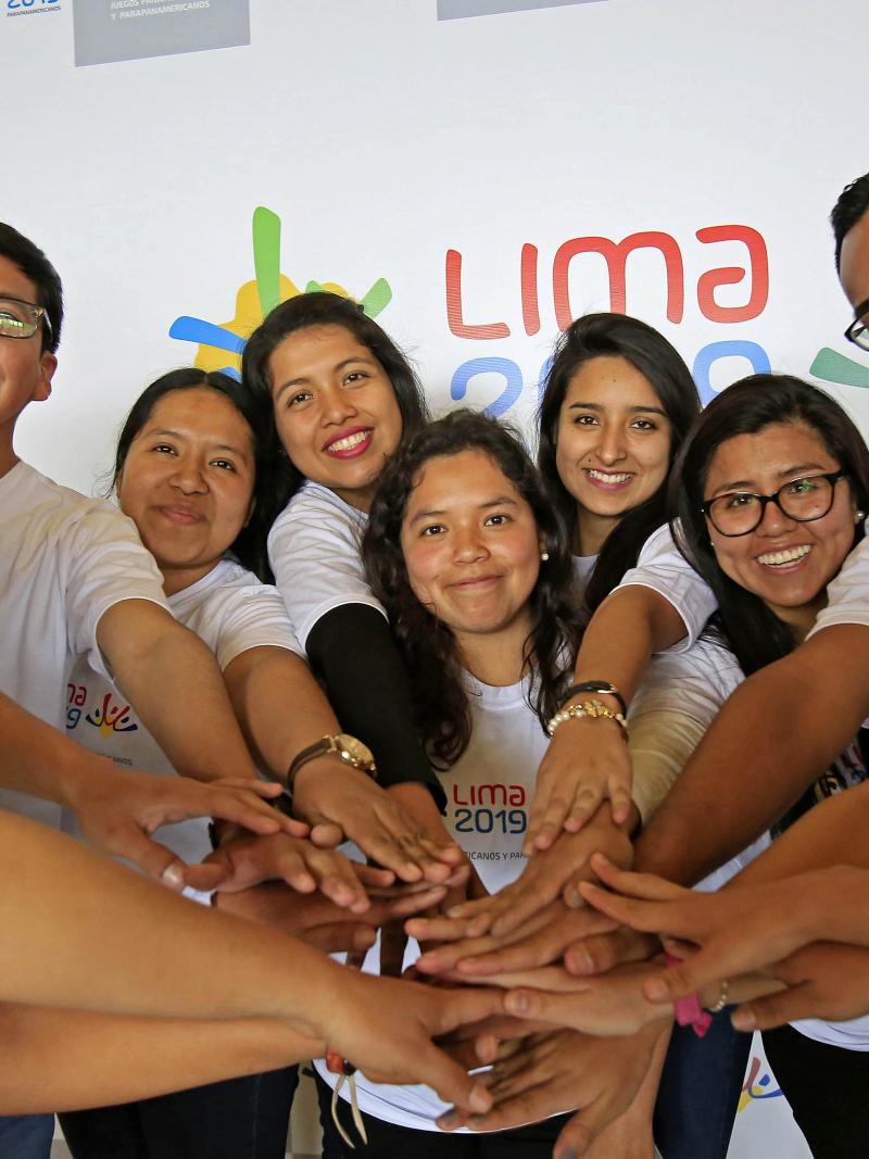 Twelve people smiling and placing their hands on each others'