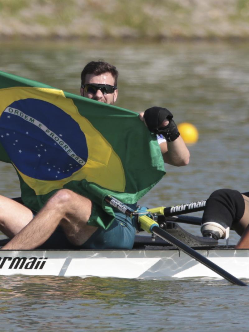 A man and woman in rowing boat celebrate, while man holds up Brazilian flag