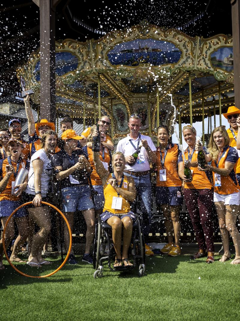 Group photo of Dutch Para equestrian team dressed in orange team colors celebrating with champagne 