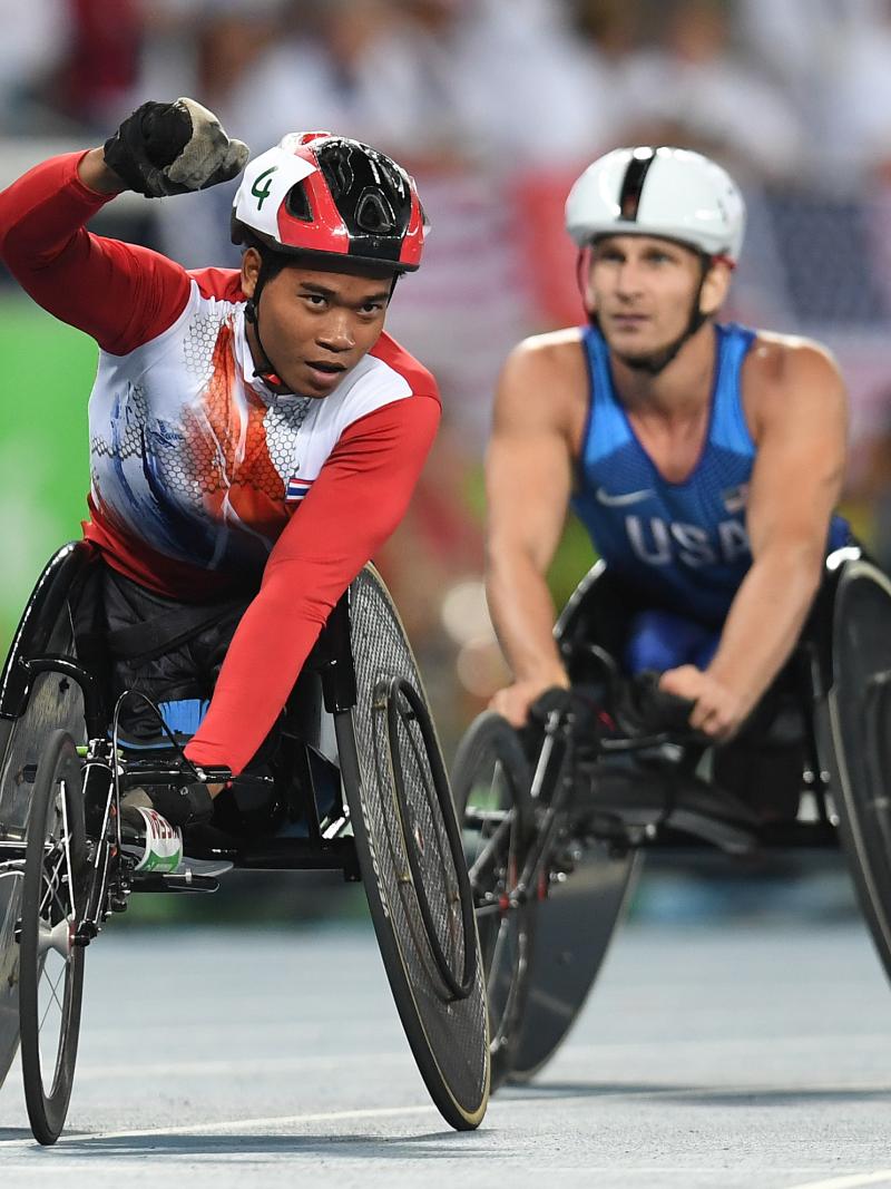 Man in a race wheelchair celebrating with another man in a race wheelchair behind him