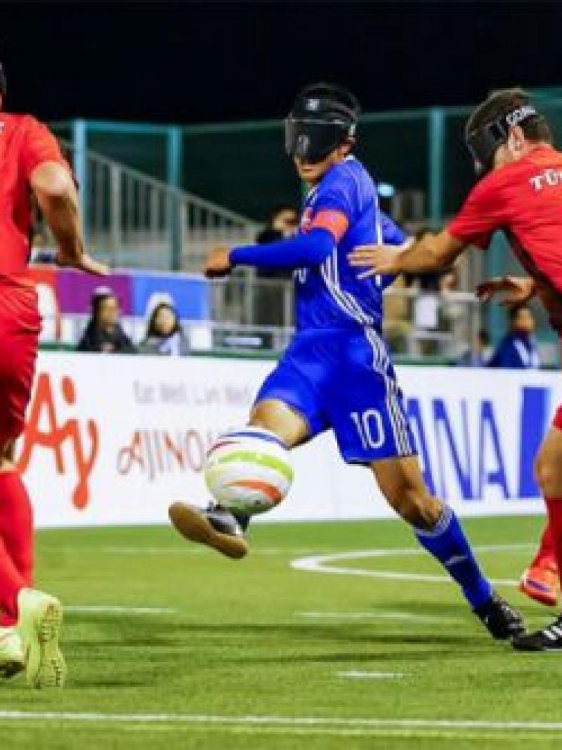 a Japanese blind footballer dribbles the ball through two opponents