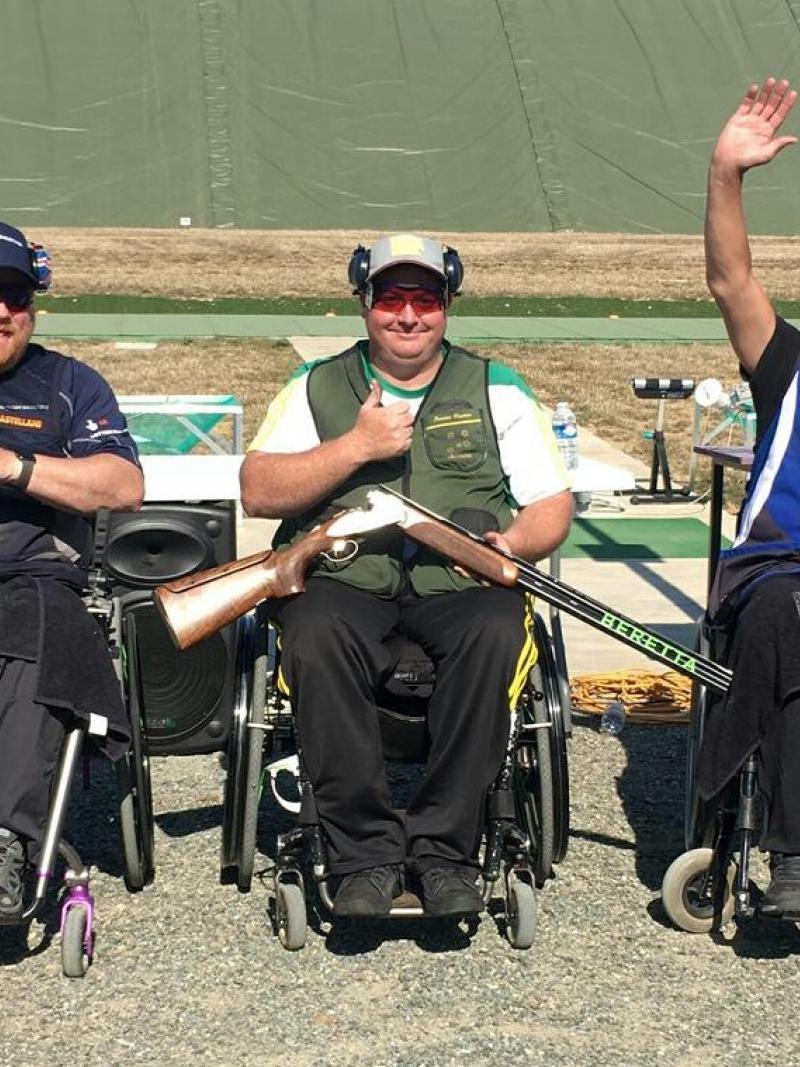 three male Para shooters in wheelchairs with Scottie Brydon in the middle waving to the crowd