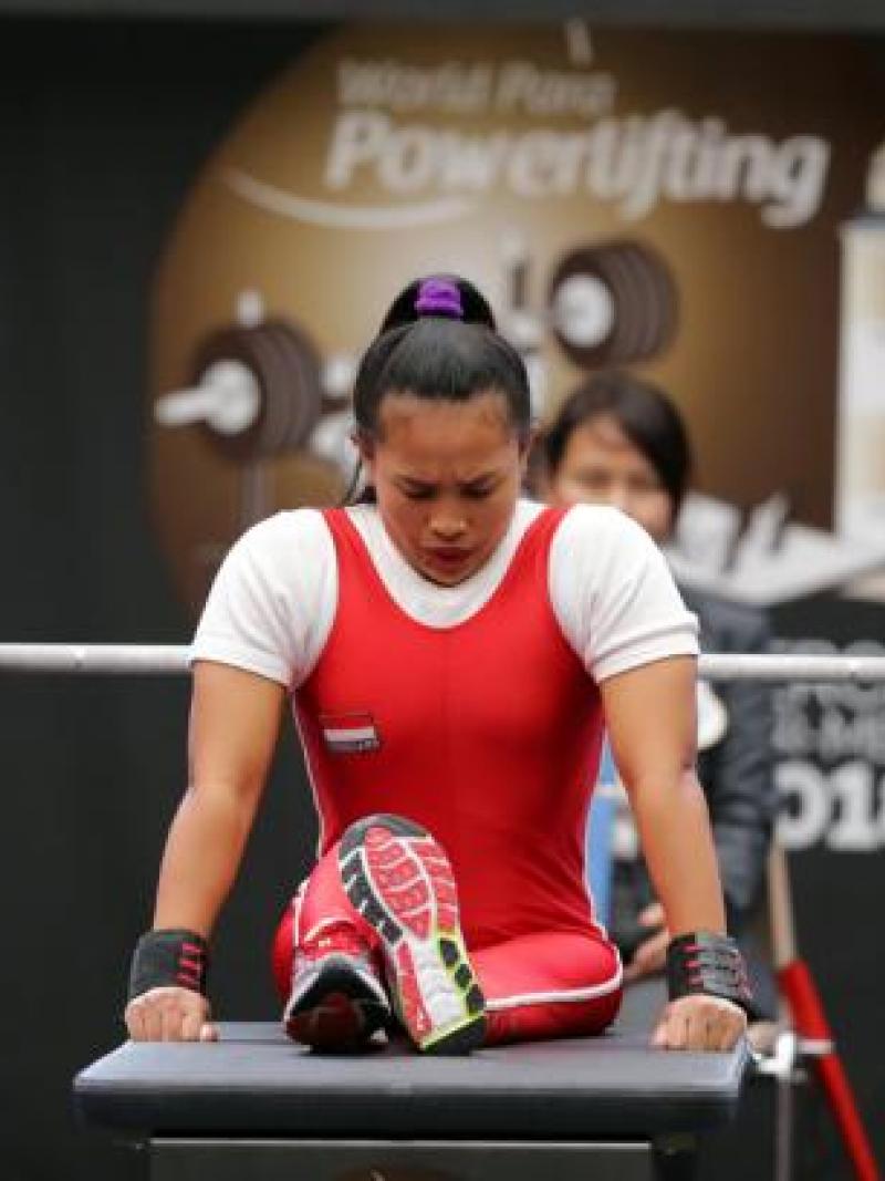 Woman bows head as she sits on powerlifting bench preparing to lift the bar