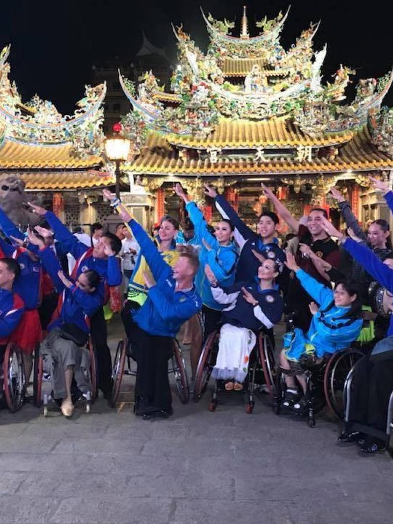 a group of Para dancers raising their arms in front of three golden Chinese temples