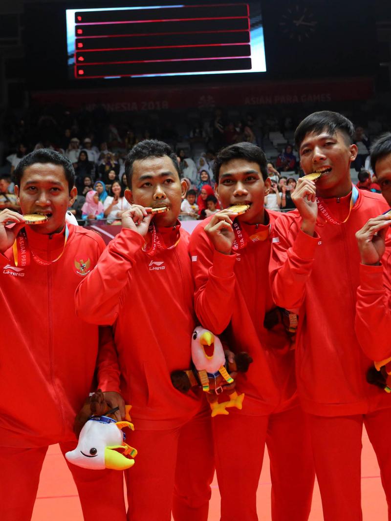 a group of Indonesian male Para badminton players biting their gold medals