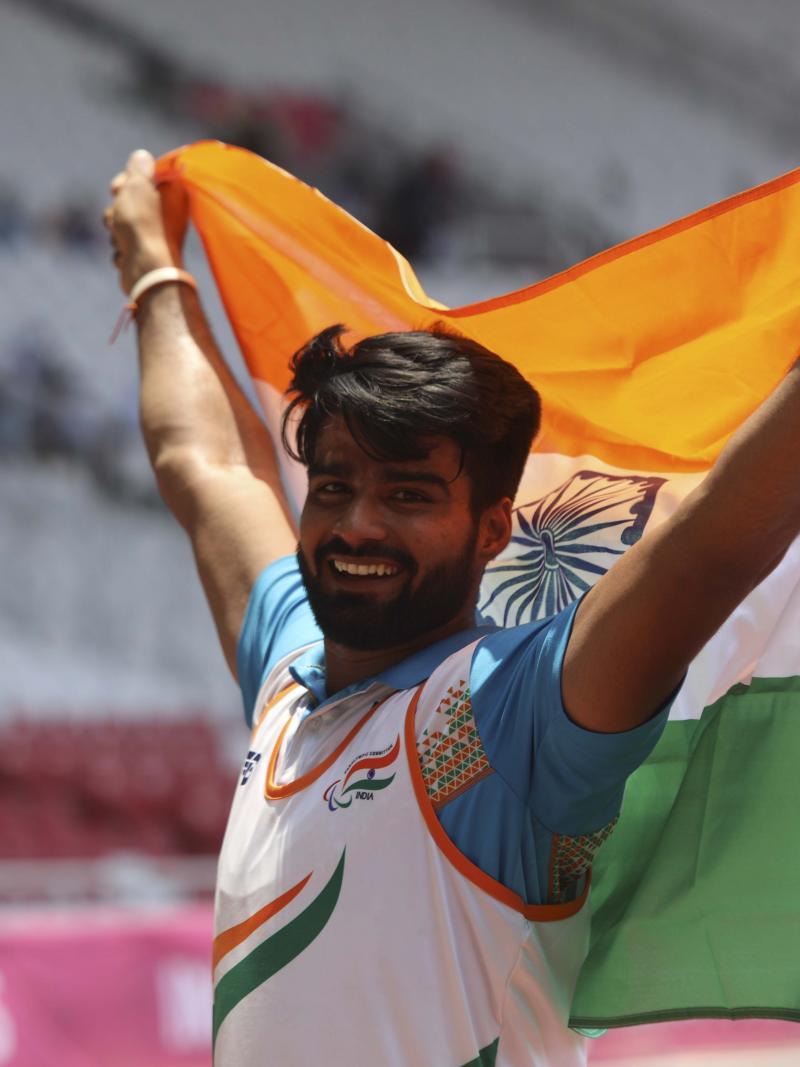 male Para athlete Sandeep Sandeep smiling and holding up an India flag