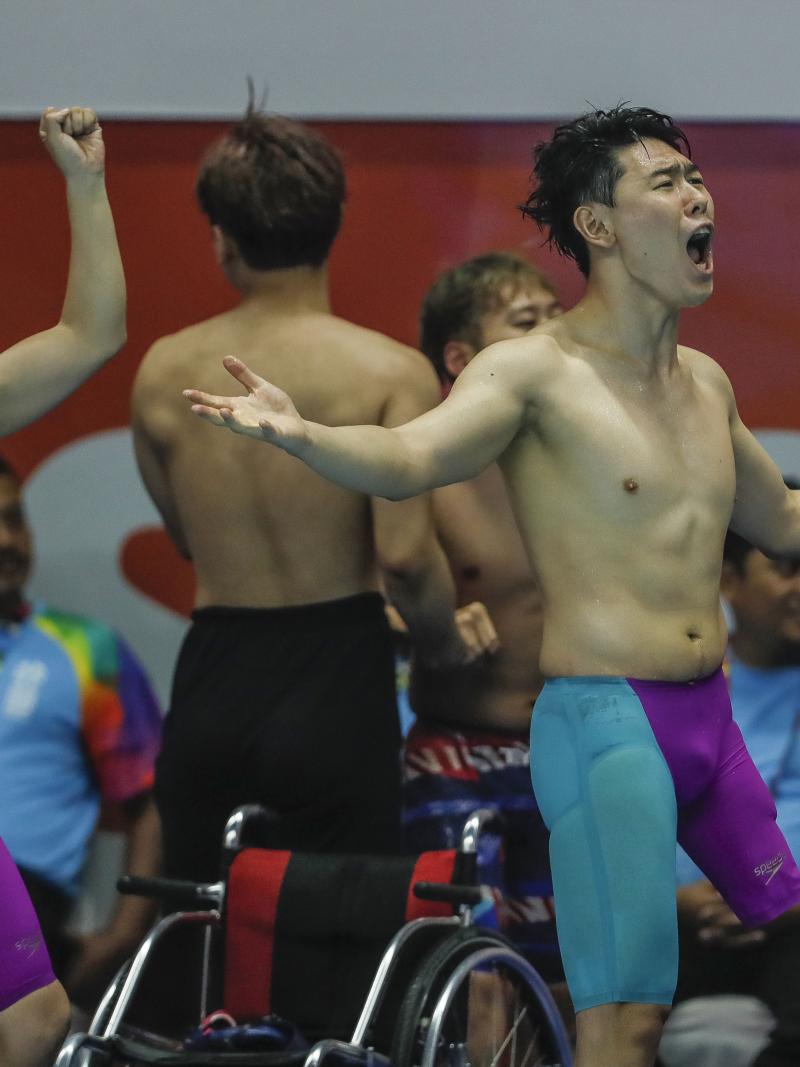 three male Para swimmers celebrate at the edge of the pool 