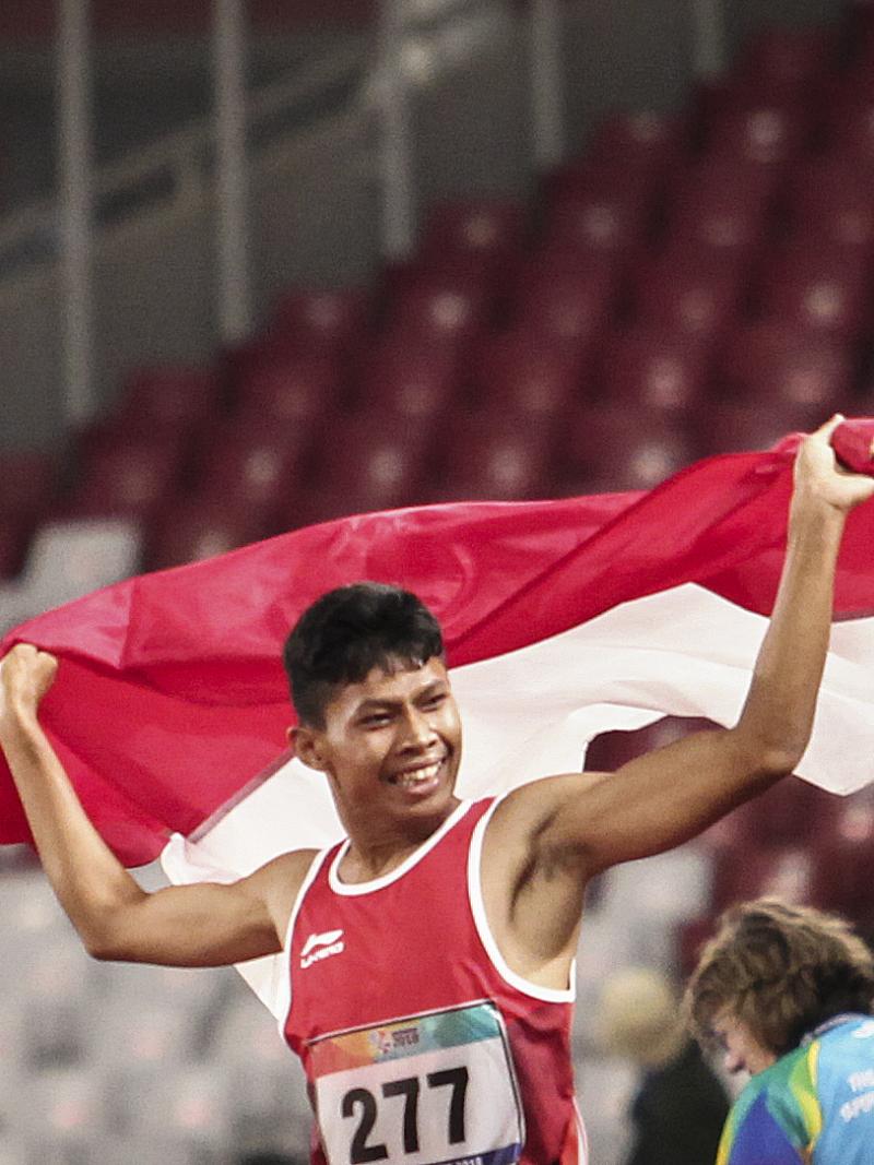 male Para athlete Sapto Yogo Purnomo running holding an Indonesia flag