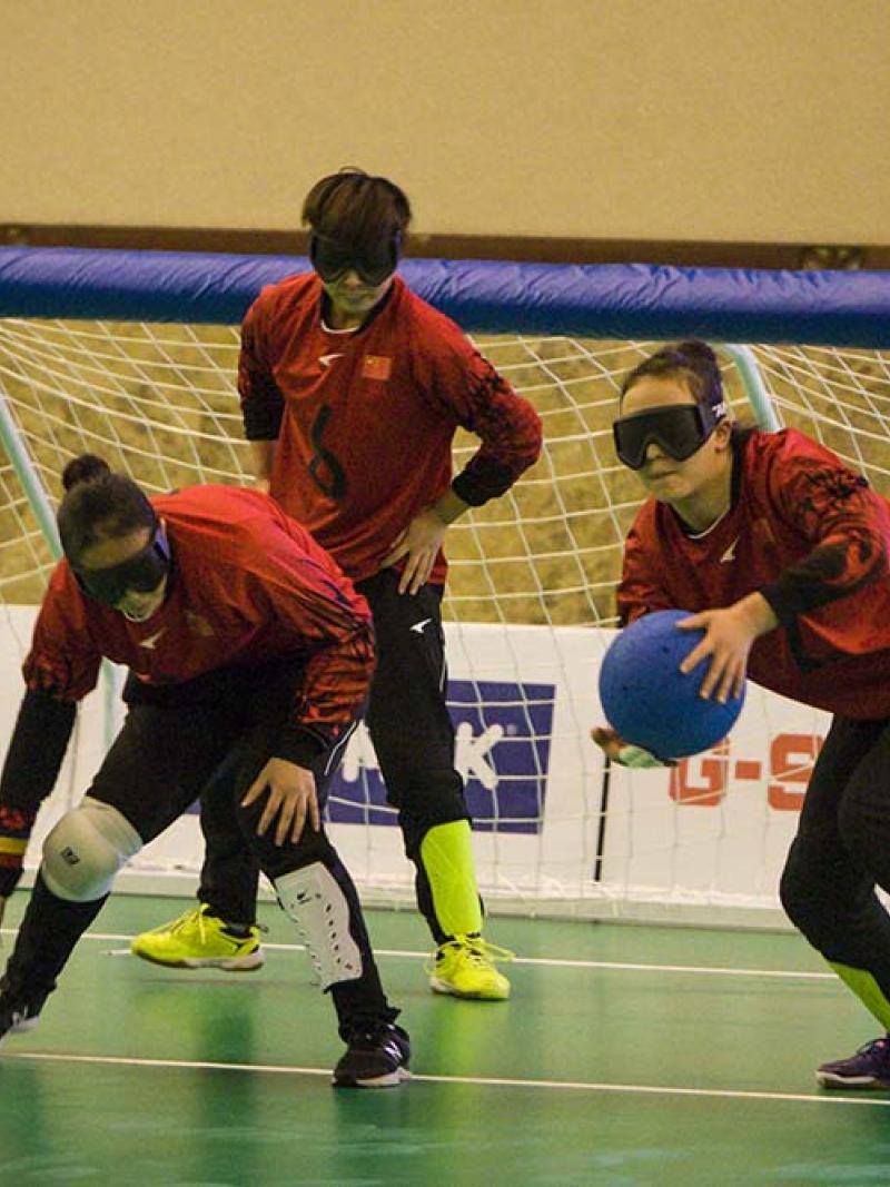 three female Chinese goalball players talking in front of the goal
