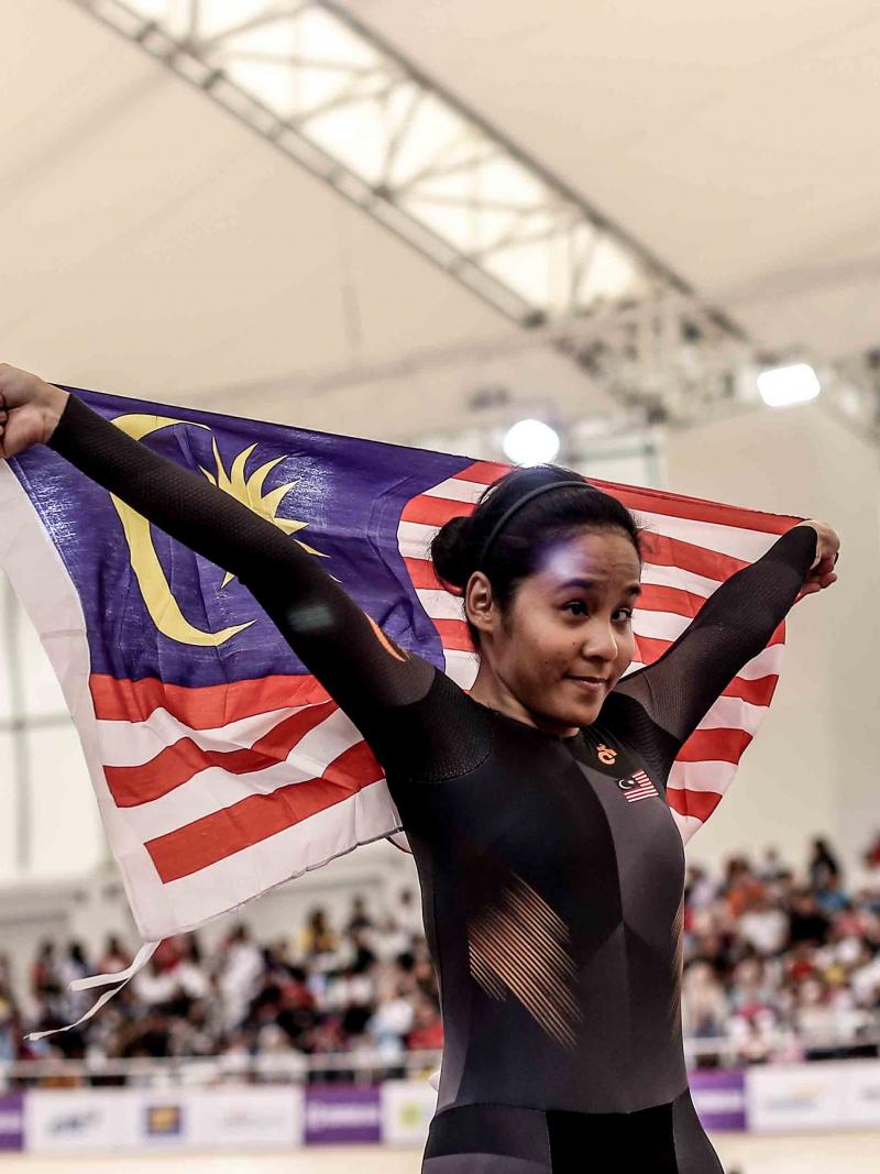 female Para cyclist Nur Azlia Syafinaz Mohd Zais holds up a Malaysia flag