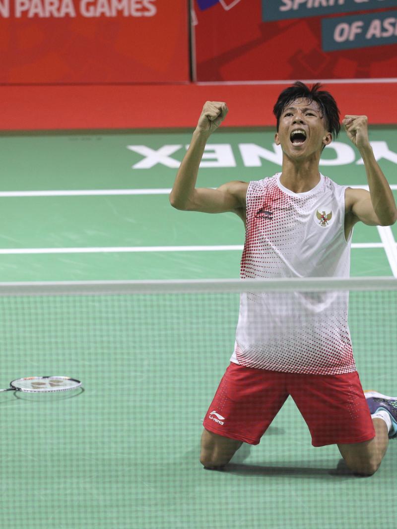 male Para badminton player Dheva Anrimusthi falls to his knees and clenches his fists on the court