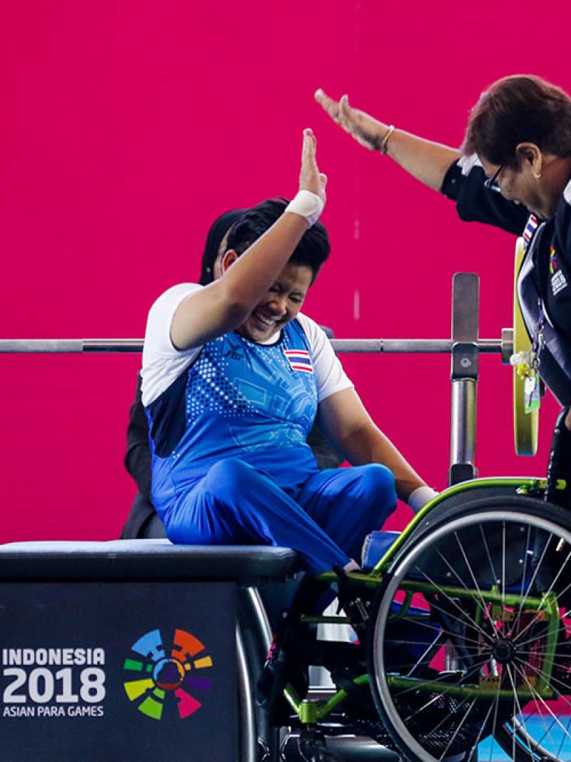 Woman powerlifter on a bench celebrating with another woman
