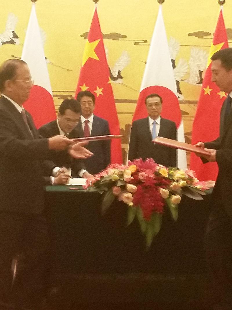 Beijing 2022 and Tokyo 2020 men in suits in a room exchanging documents