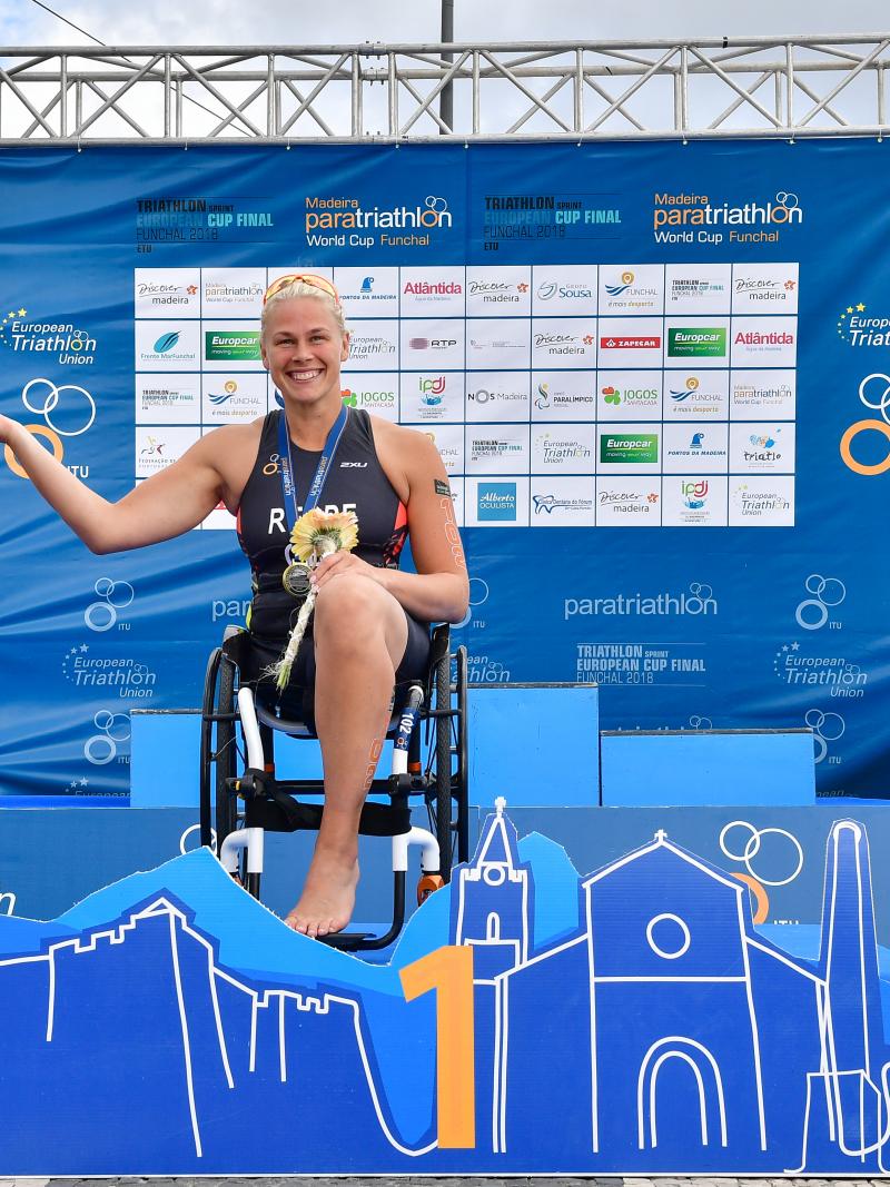 female Para triathlete Christiane Reppe holds the hand of another female athlete on the podium