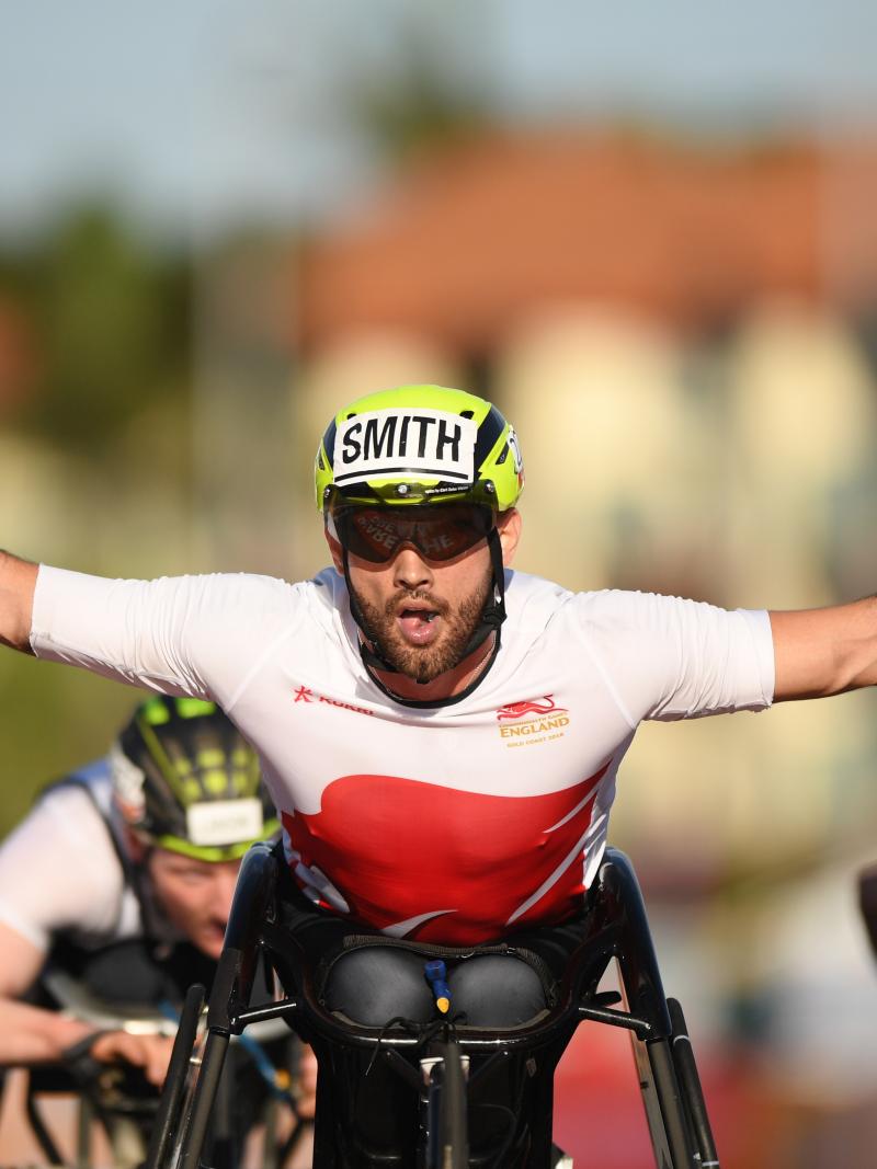 male wheelchair racer Johnboy Smith raises his arms wide as he crosses the finish line